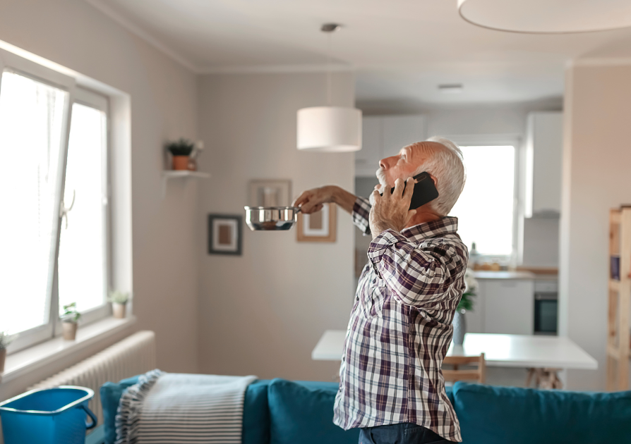 man holding bowl to catch ceiling water leak while on the phone