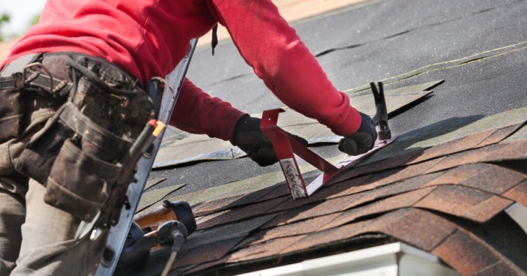 A worker replacing shingles on a roof.