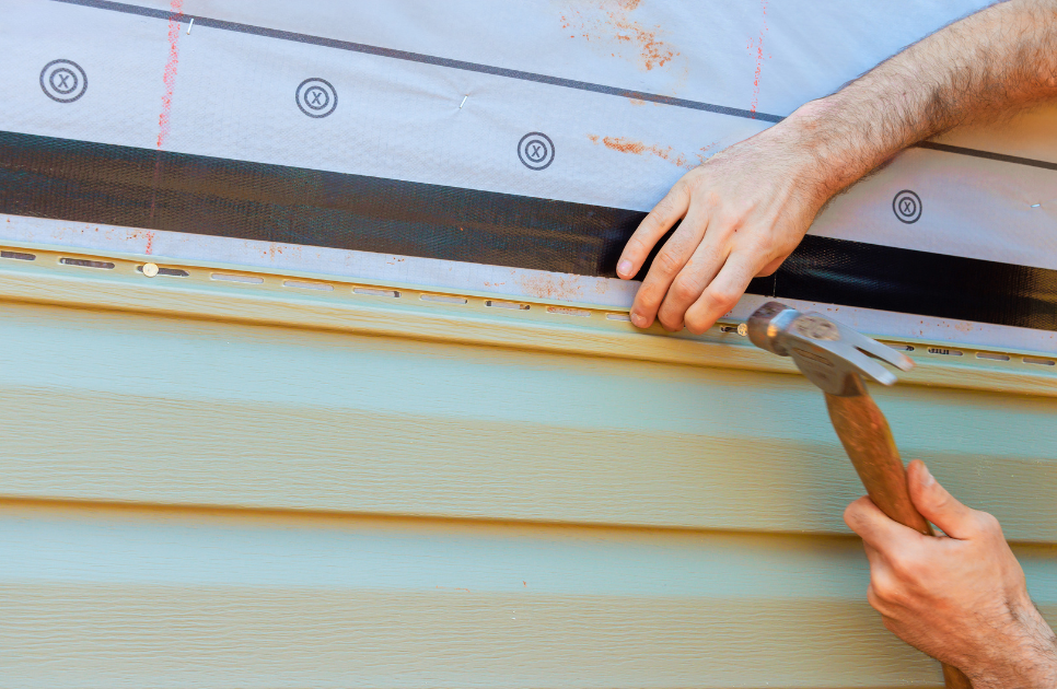 man nailing siding panels on home