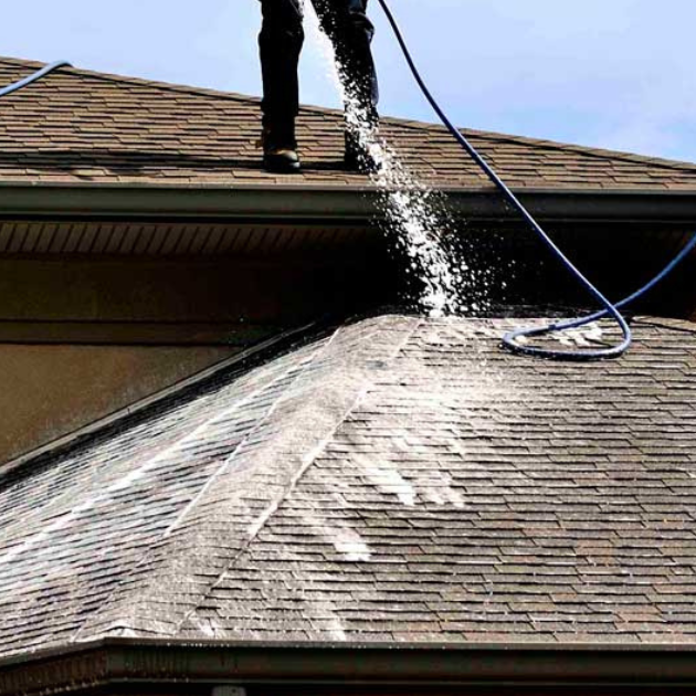 man washing roof with a hose