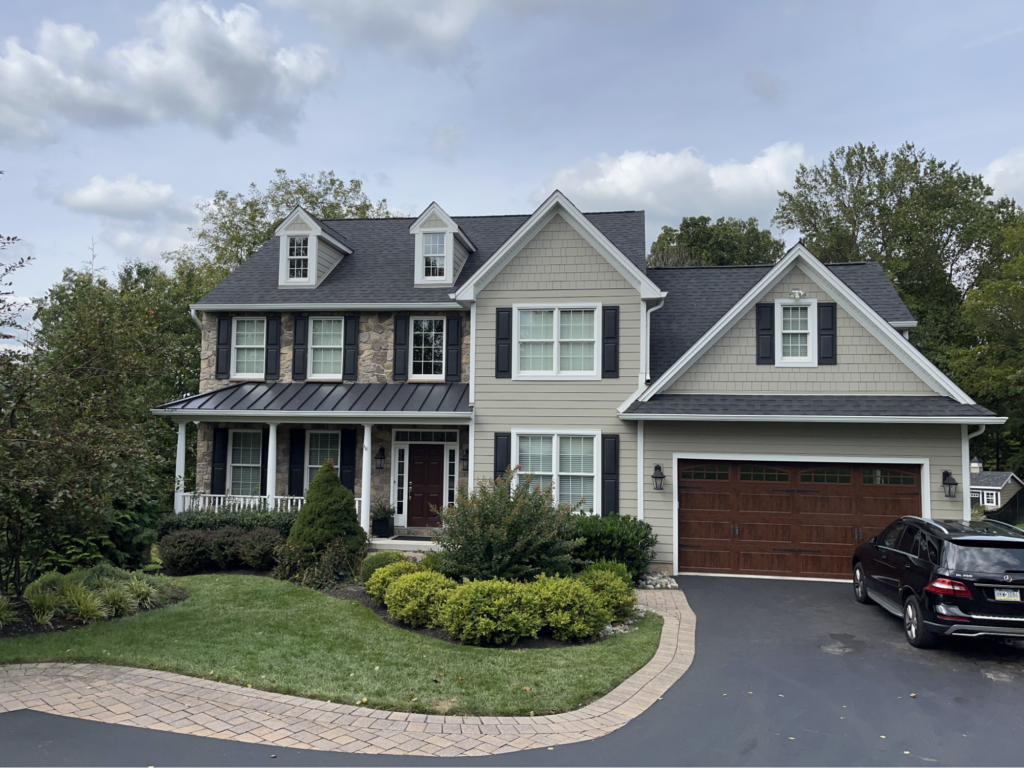 Cozy two-story home with stone accents and a winding driveway. A small metal roof if above the front patio and grey asphalt shingles cover the rest of the house.