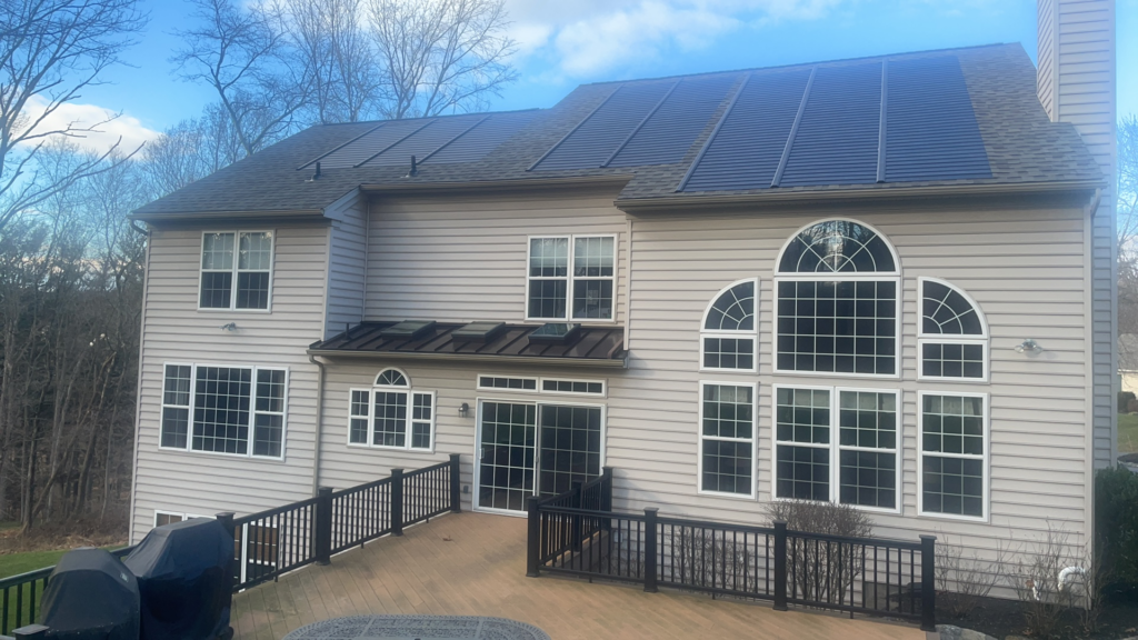 Exterior shot of a beige panel, two-story home with small metal roof featuring skylights above the patio and solar shingles lining the main roof roofer.