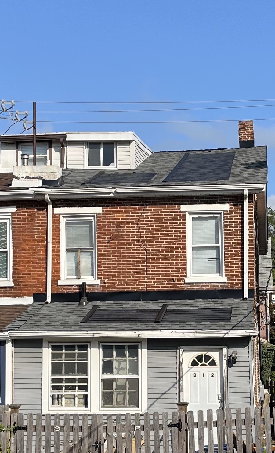 A row home with solar shingles are 2 levels of the black asphalt roof and a blue sky above.
