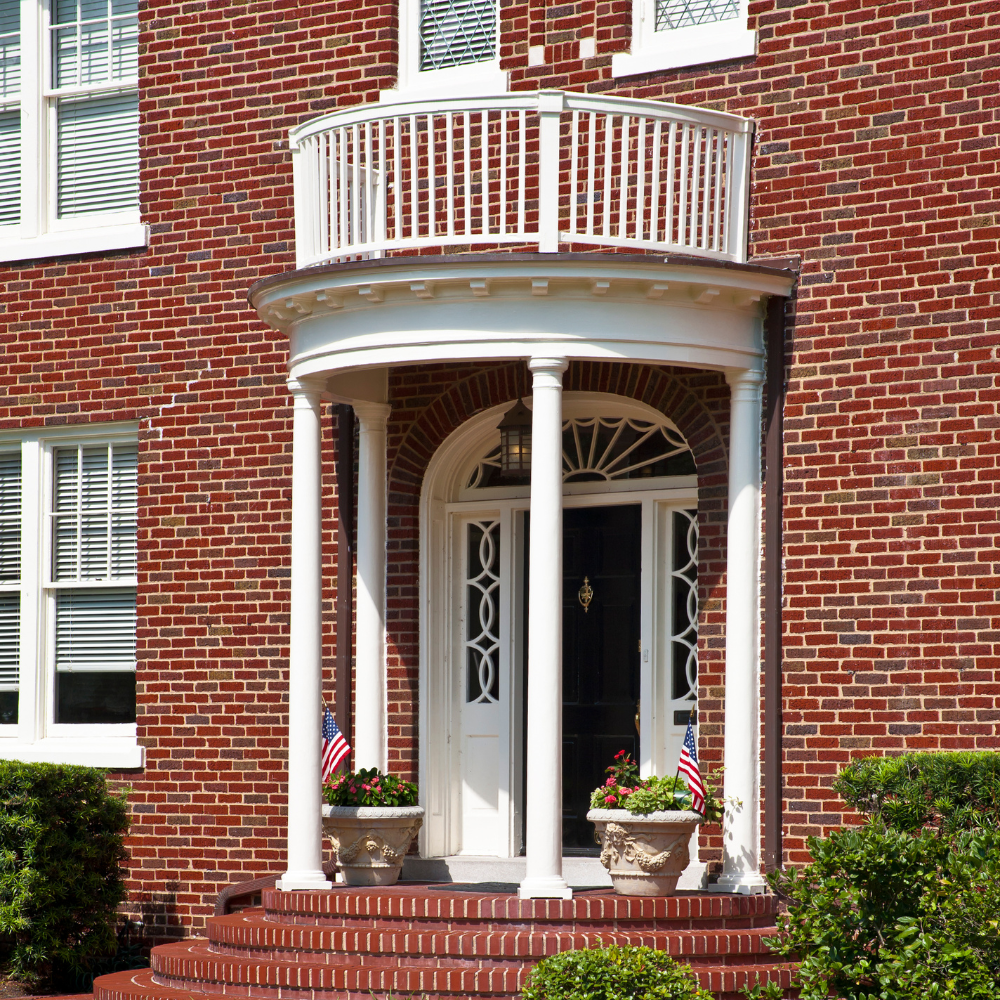 semi circle portico with thin columns and a balcony on top on a red brick home