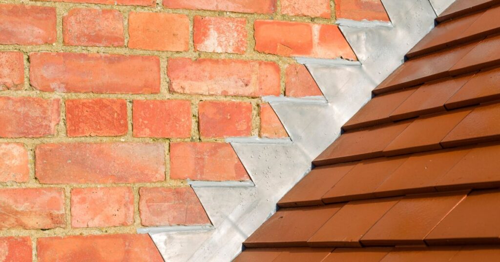 Flashing between deep brown shingles, and brick wall/portion of roof.